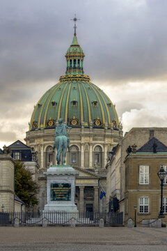 View of Frederik's Church with its iconic green copper dome and the equestrian statue of King Frederik V in the foreground, set against a cloudy sky in Kobenhavn, Denmark.