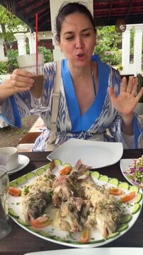 Woman holding iced coffee and talking at outdoor restaurant during lunch with seafood dishes