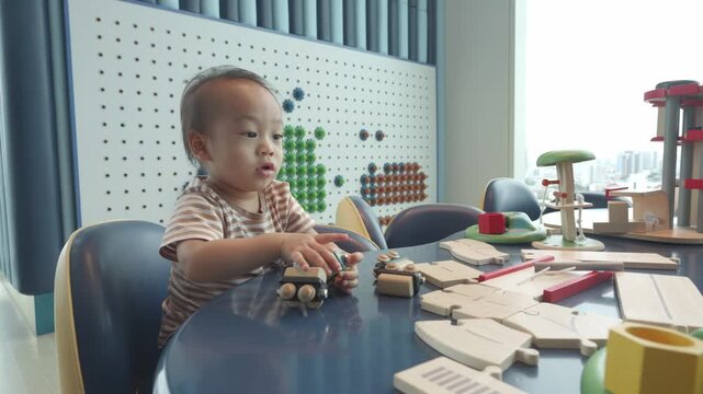 A young child engages in imaginative play at a vibrant table filled with toys. The playful environment encourages creativity and fun learning, featuring a bright backdrop and various stimulating objec