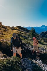 Man and child descend a rocky mountain path with backpacks under a bright sky. Guided family hiking on rugged terrain for adventure travel and outdoor parenting themes © Екатерина Лукашина