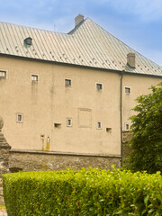 Historic castle wall with green bushes. A castle wall stands tall with small windows under a blue sky. Green bushes grow in front of the wall. © Daniil