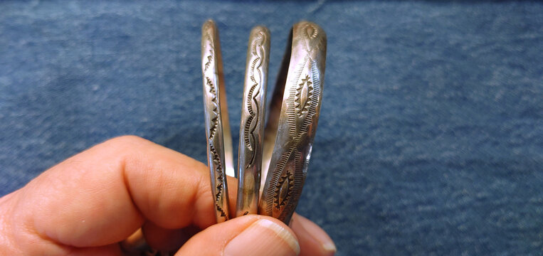 Three handheld Antique Navajo or Hopi silver bracelets with indigo color cloth background