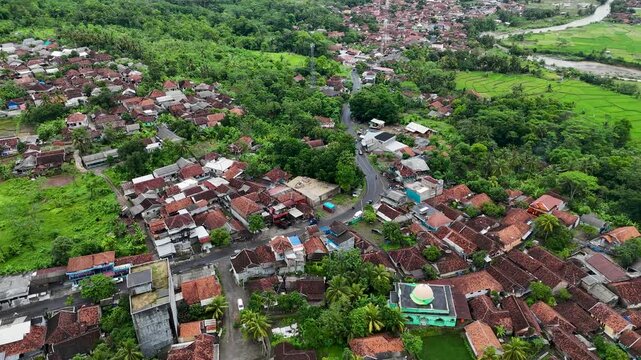 Aerial view of Lio citarik village with traditional houses, lush green trees, a mosque with a green dome, and winding roads in Kecamatan Pelabuhanratu, Jawa Barat, Indonesia.