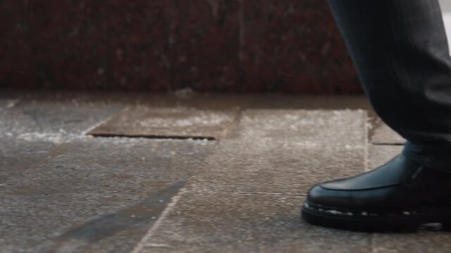 Close up of man black leather shoes walking on wet stone pavement capturing movement and texture details. scene focuses solely on foot motion against urban outdoor background with no other