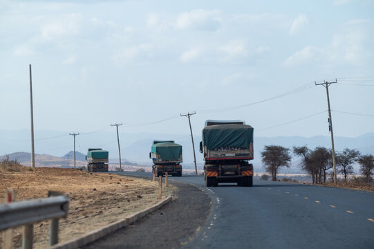 View of three trucks driving along a paved road in Amboseli National Park, Kajiado County, Kenya.