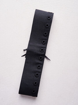 Black fabric cuff with reinforced stitched eyelets on neutral background.