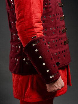 Red and burgundy brigandine sleeve and torso armor with metal rivets on reenactor&rsquo;s arm.