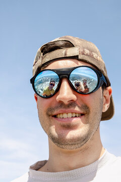 Man smiling with friends reflected in sunglasses on Pyrenees summit