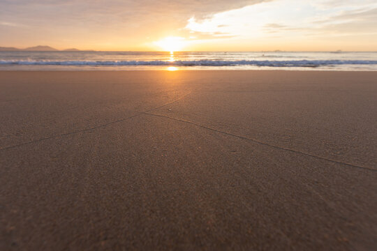 Empty beach at sunset with wet sand and subtle lines leading to the glowing horizon, calm waves and a warm golden atmosphere evoking peace, solitude and coastal serenity. Cam Ranh, Vietnam