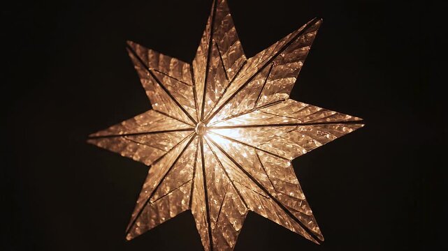 L&aacute;mpara en forma de estrella navide&ntilde;a de ocho puntas que emite una c&aacute;lida luz dorada y gira lentamente sobre un fondo oscuro, proyectando destellos.