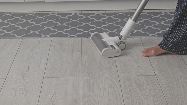 Homemaker is employing a cordless stick vacuum cleaner to tidy up the wooden floors. This modern household tool is essential for everyday cleaning tasks