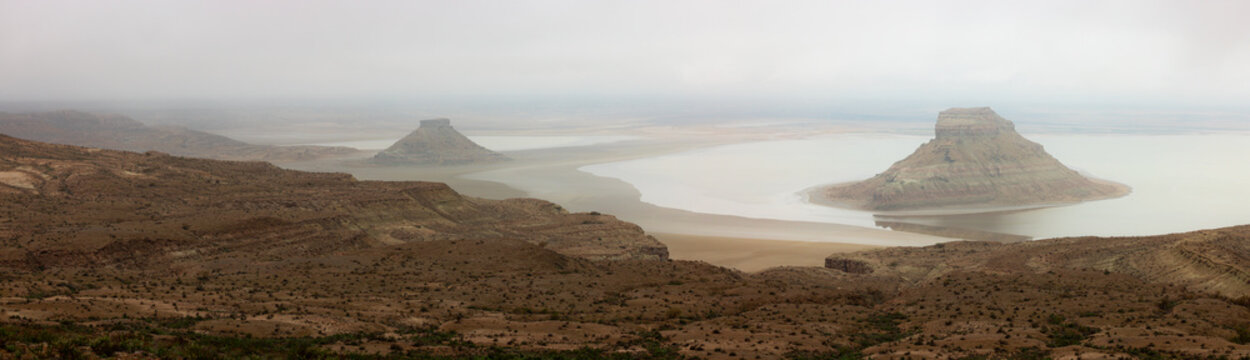View of the Karynzharyk depression with its distinctive isolated rock formations rising from the salt flats under a cloudy sky in Karakiya District, Mangystau Region, Kazakhstan.