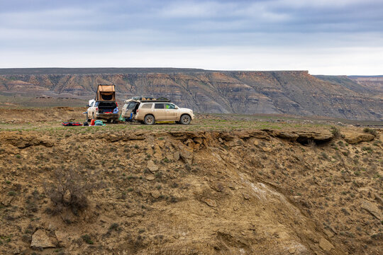 View of off-road vehicles with rooftop tents parked on the edge of a rocky cliff overlooking the vast arid landscape of Karynzharyk in Karakiya District, Mangystau Region, Kazakhstan.