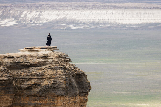 View of a person in black clothing standing on the edge of a rocky cliff overlooking the vast desert landscape of Bozjyra in Aktau, Mangystau Region, Kazakhstan.