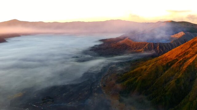 Aerial view of Mount Bromo volcanic crater surrounded by a sea of clouds at golden hour in Tosari, East Java, Indonesia.