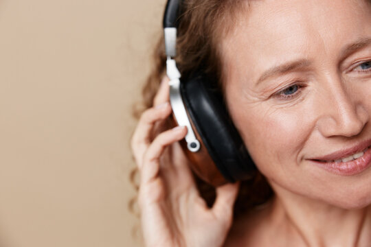 A middle aged woman wearing headphones smiles softly, closeup in a warm light, showcasing authentic skin and natural beauty without retouching.