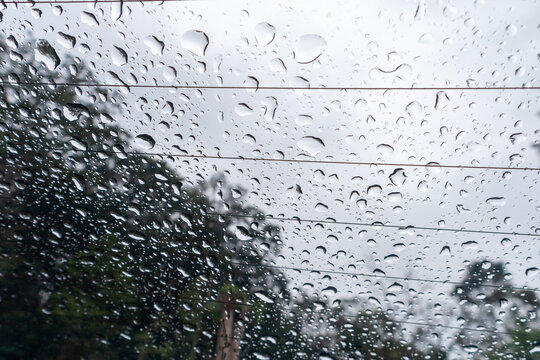 Raindrops collecting on car rear glass window with defroster lines during heavy rain