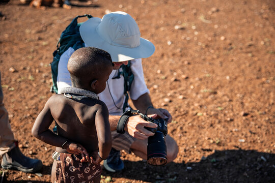 Himba child watching tourist reviewing camera images in Namibia