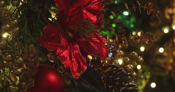 Red poinsettia flower and ornaments hanging on decorated Christmas tree with warm bokeh lights, festive holiday interior background, commercial seasonal .