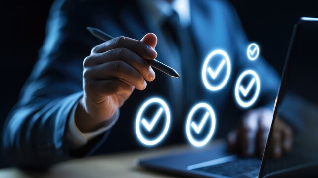 A businessman points a stylus pen toward glowing check mark icons near a laptop in a dark office. This digital quality assurance concept is ideal for technology and compliance.