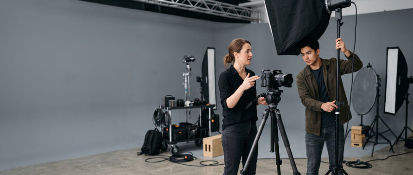 Professional photographer and assistant plan creative shoot in studio, coordinating camera setup, lighting and production workflow during collaborative commercial photography session with copy space.