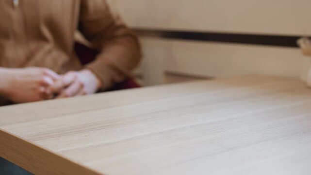 Close up of man hands resting on wooden table fingers interlaced with one black ring visible. scene is calm and stationary throughout focusing solely on hand position against blurred