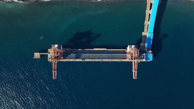 Aerial view of the Celukan Bawang Steam Power Plant jetty with industrial cranes extending into the sea in Buleleng, Bali, Indonesia.