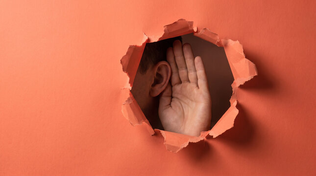 Market research and consumer insight concept showing an ear listening intently through a torn orange paper background