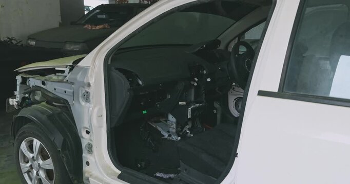 Abandoned white car with missing parts sitting in dusty underground parking lot, damaged interior and exterior, urban decay and vandalism context, documentary .