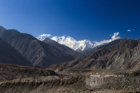 View of the snow-capped Nanga Parbat mountain peak rising above rugged, rocky mountain ranges under a clear blue sky in Thalichi, Gilgit Baltistan, Pakistan.