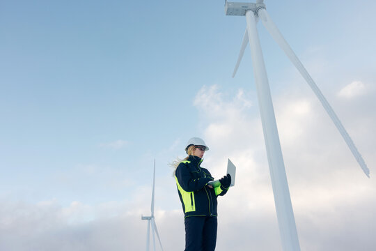 Woman engineer inspecting wind turbines in a snowy, cold environment with a laptop