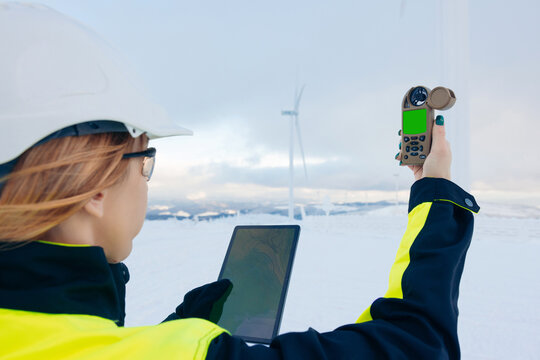 Wind energy technician uses tablet and anemometer in snowy landscape