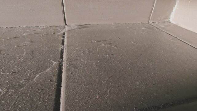 Detailed view of a very dusty and dirty tiled floor. Grime, cobwebs, and hair accumulated in the corner and along the grout lines