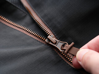 A close-up shot of a hand unzipping a black waterproof jacket with brown zipper details. © Stepan Popov