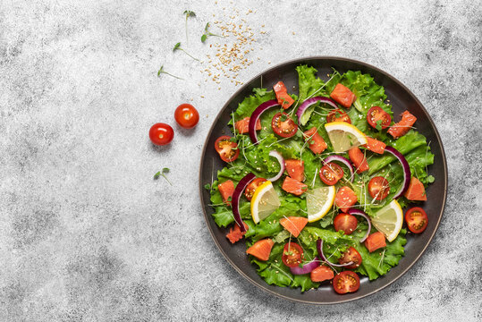 Diet salad with salmon and fresh vegetables on light grunge background, top view, flat lay, copy space.