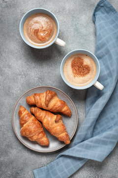 Two cups of coffee and fresh croissants on gray grunge background, top view, heart pattern on coffee, Valentine's Day