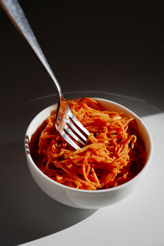 Vibrant carrot noodles in a white bowl with a metal fork, highlighted by dramatic light and shadow. A fresh, healthy, appetizing dish perfect for health, lifestyle, and recipe visuals.