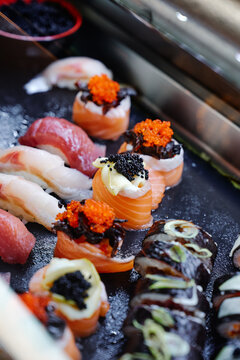 An assorted sushi platter featuring salmon nigiri, maki rolls and vibrant orange and black fish roe arranged on a black slate serving board for an elegant, gourmet presentation.