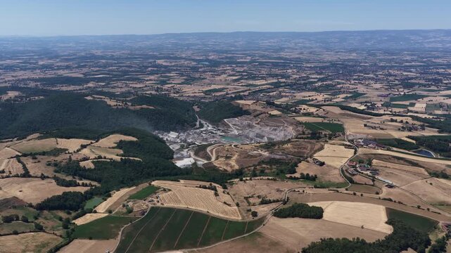 Wide aerial of large quarry green forests golden fields and expansive rural landscape under clear sky