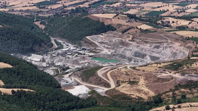 Close aerial of active quarry turquoise pond industrial buildings green forest and dusty roads
