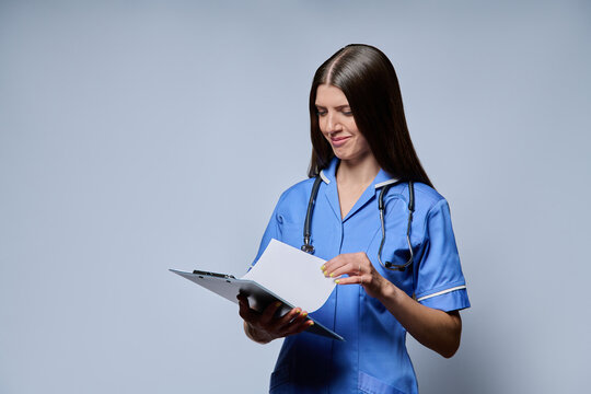 Female nurse turning page on clipboard reading patient records against grey background