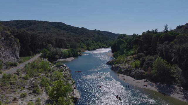 Aerial of sparkling river with canoes swimmers sandy beaches forested hills and road under clear sky