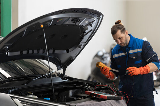 Male mechanic diagnosing battery under hood of car at the garage. Mechanic examining, repair and maintenance automotive electrical systems at auto car repair service