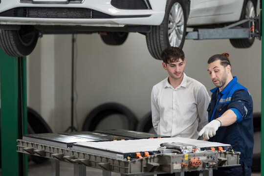 Electric vehicle car auto services. EV garage. Diagnostic battery pack. Customer and mechanic discussion and diagnosing electric car vehicles battery, component checks at auto workshop