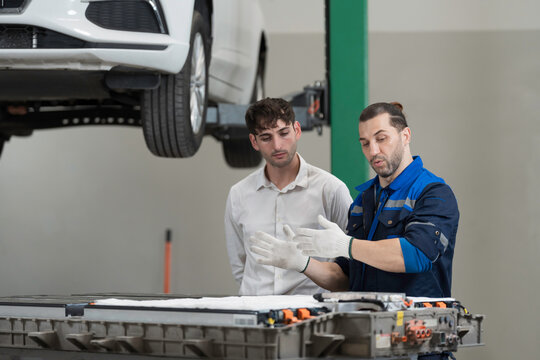 Electric vehicle car auto services. EV garage. Diagnostic battery pack. Customer and mechanic discussion and diagnosing electric car vehicles battery, component checks at auto workshop