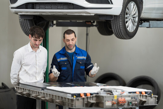 Electric vehicle car auto services. EV garage. Diagnostic battery pack. Customer and mechanic discussion and diagnosing electric car vehicles battery, component checks at auto workshop