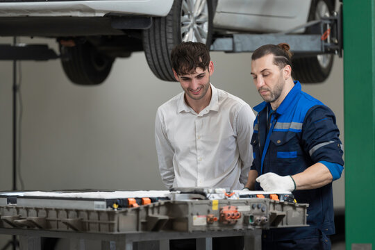Electric vehicle car auto services. EV garage. Diagnostic battery pack. Customer and mechanic discussion and diagnosing electric car vehicles battery, component checks at auto workshop