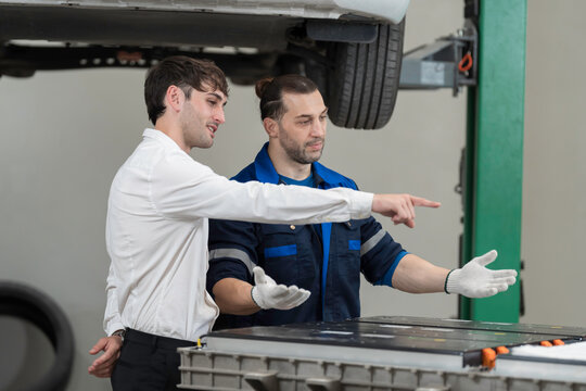 Electric vehicle car auto services. EV garage. Diagnostic battery pack. Customer and mechanic discussion and diagnosing electric car vehicles battery, component checks at auto workshop