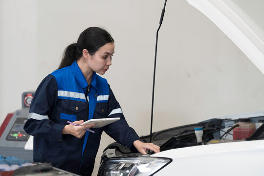 Female mechanic working at the garage. Female car mechanic examining, repair and maintenance under hood of car at auto car repair service. Car service and Maintenance concept