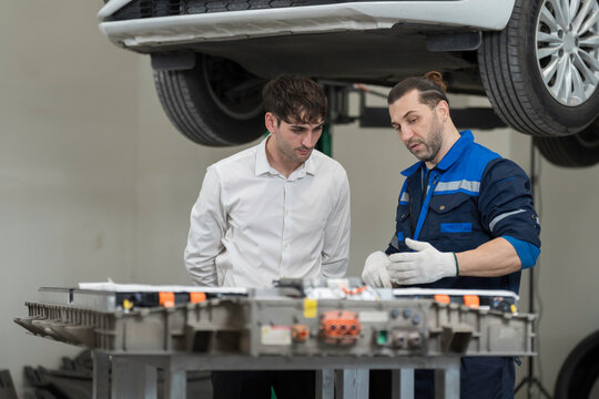Electric vehicle car auto services. EV garage. Diagnostic battery pack. Customer and mechanic discussion and diagnosing electric car vehicles battery, component checks at auto workshop